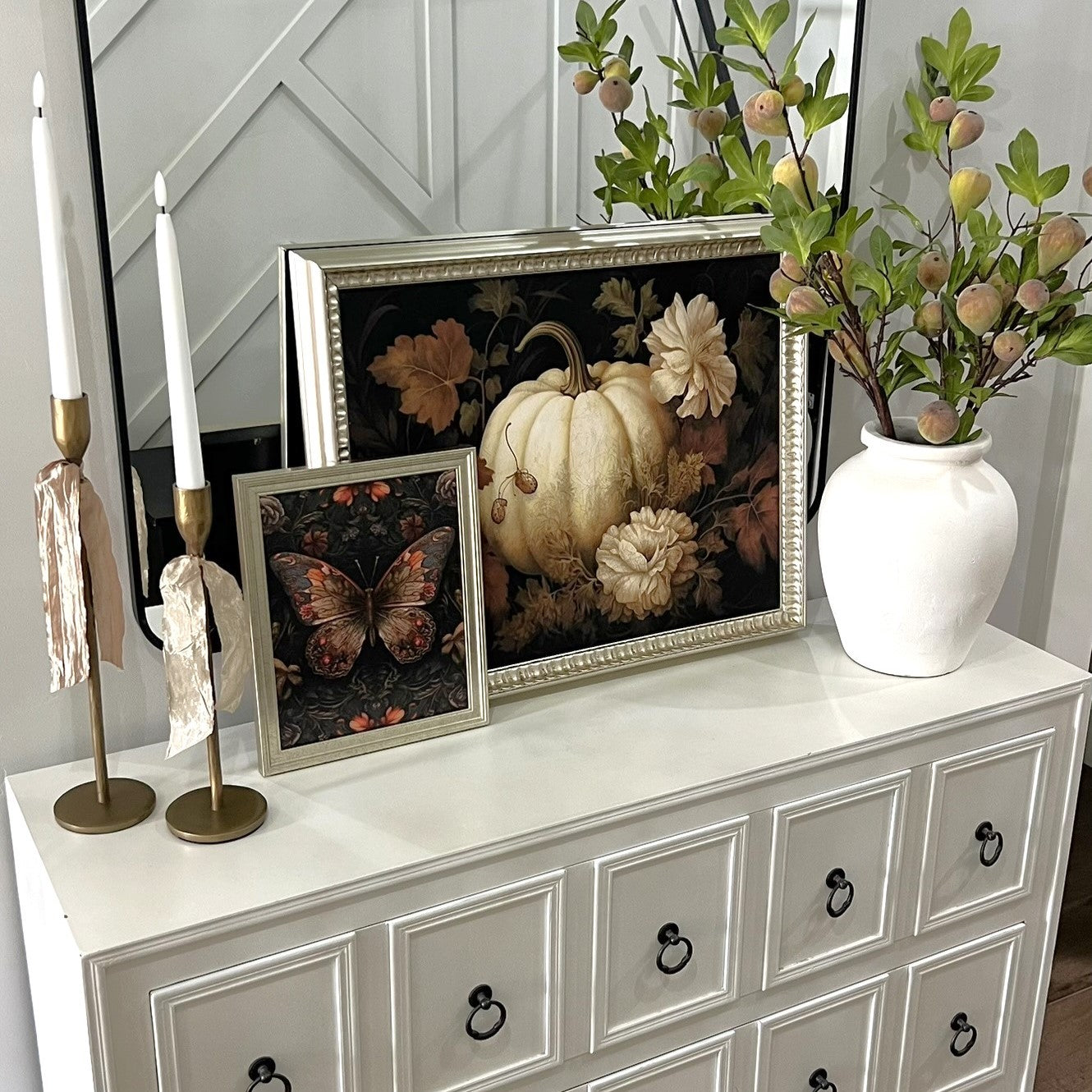 Decorative items on a white dresser including framed pictures, a vase with flowers, and candles.