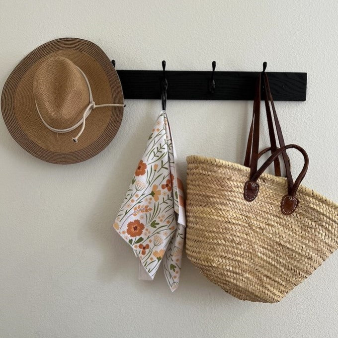Hat, floral towel, and woven bag hanging on a black wall hook against a white wall.