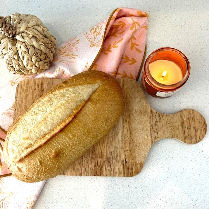 Loaf of bread on a wooden cutting board with a candle and decorative items on a light background