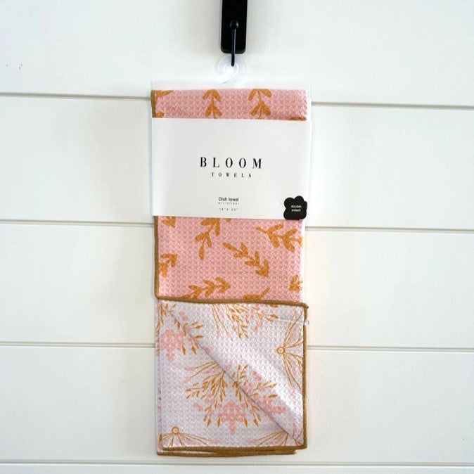 Packaged towel with floral design and 'Bloom' branding on a white wooden background