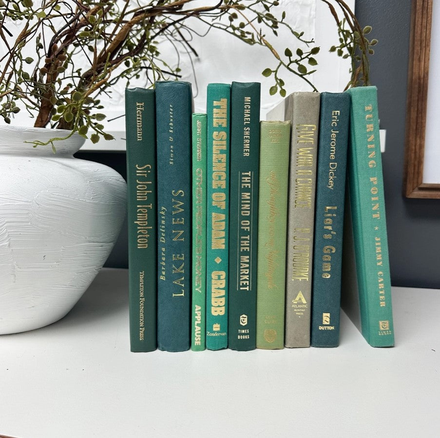 A collection of decorative books with green covers displayed on a shelf, with a decorative item partially visible to the left.