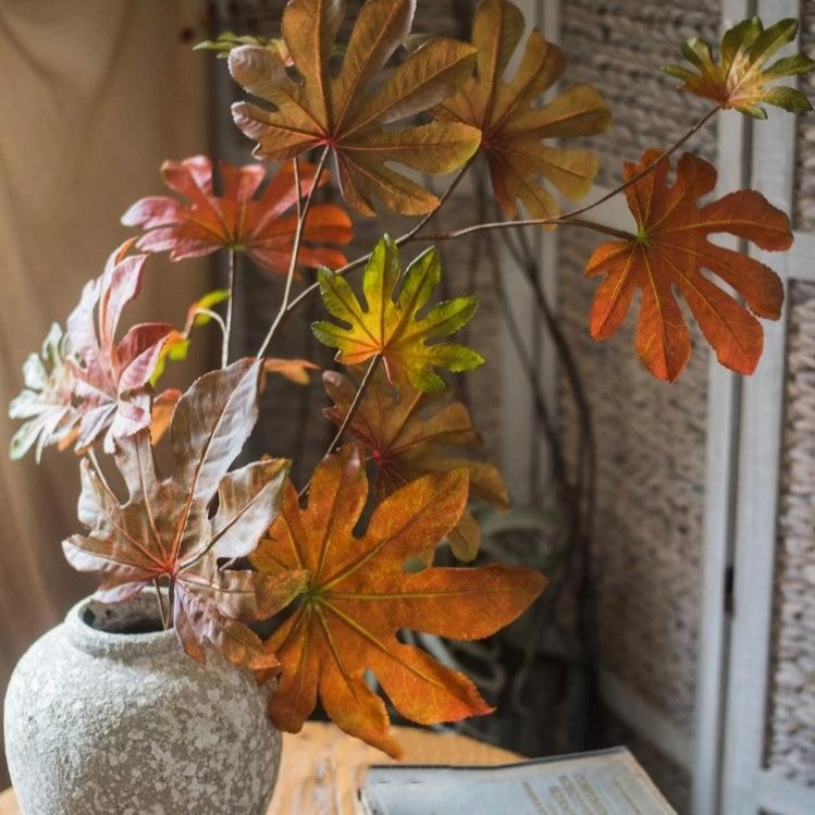 Decorative plant with autumn-colored leaves in a textured pot on a wooden surface.