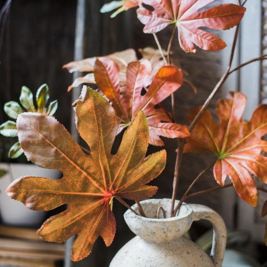 Decorative plant with autumnal leaves in a textured vase against a blurred indoor background
