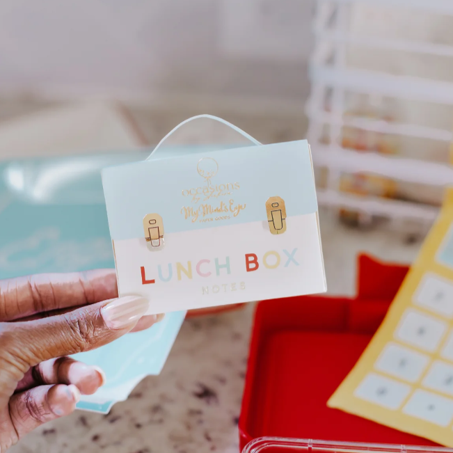 Hand holding a lunch box label with colorful text and icons.