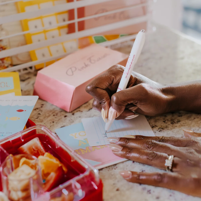 Hand writing on a piece of paper with a pen, surrounded by stationery items.