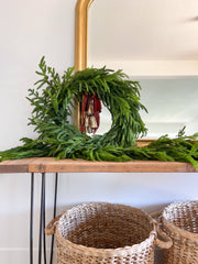 Green wreath on a wooden shelf with wicker baskets below, against a white wall.