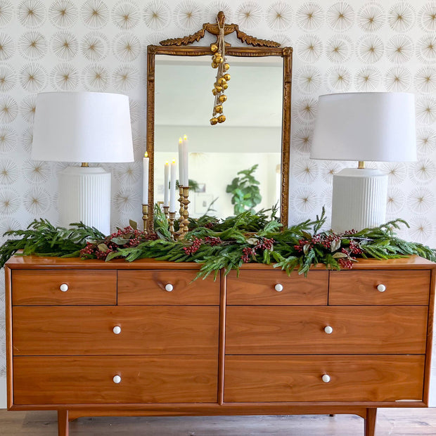 Wooden dresser with decorative mirror and greenery against a patterned wall.