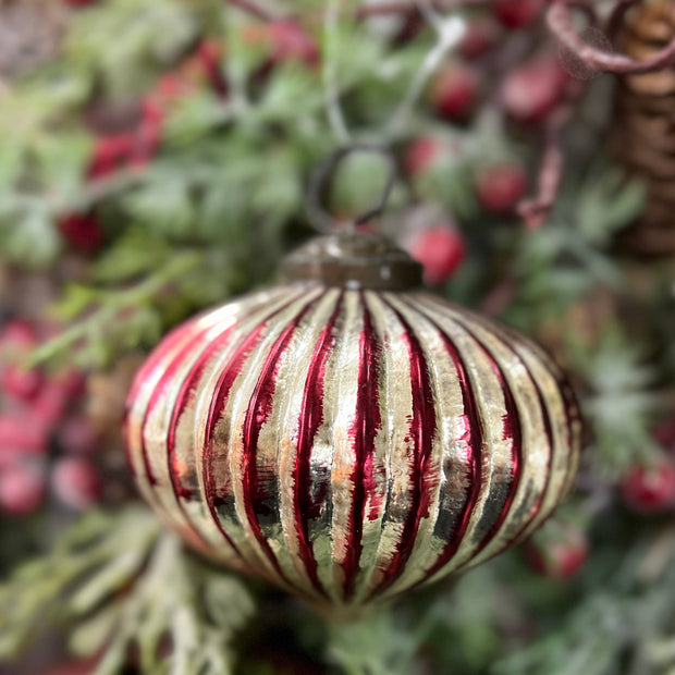 Decorative striped Christmas ornament hanging on a tree with greenery and berries.