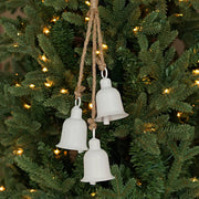 White bells hanging on a Christmas tree with lights.