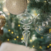 Decorative clear glass Christmas ornaments on a tree with blurred lights in the background