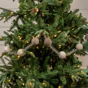 Decorated Christmas tree with lights, ornaments, and pinecones against a neutral background