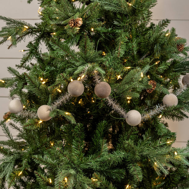 Decorated Christmas tree with lights, ornaments, and pinecones against a neutral background