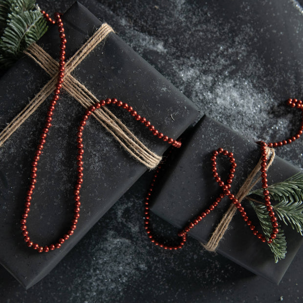 Black gift box with red beads and greenery on a dark textured surface