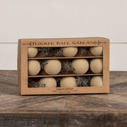 Box of 'Flocked Ball Garland' with beige balls and decorative elements on a wooden surface.