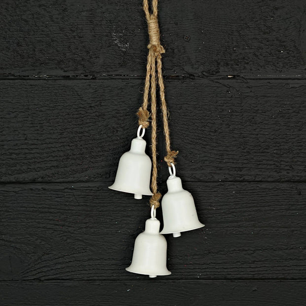Three white metal bells hanging on a rope against a black wooden background