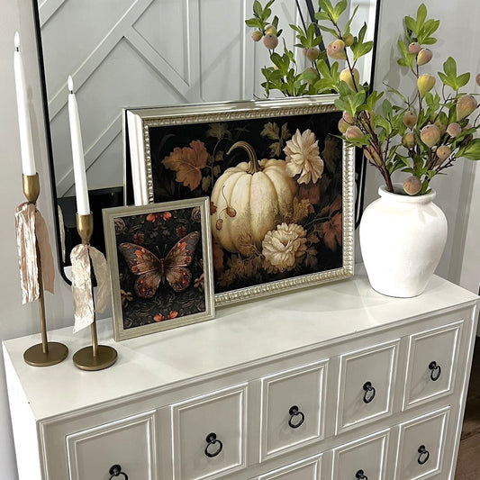 Decorative items on a white dresser including framed pictures, a vase with flowers, and candles.