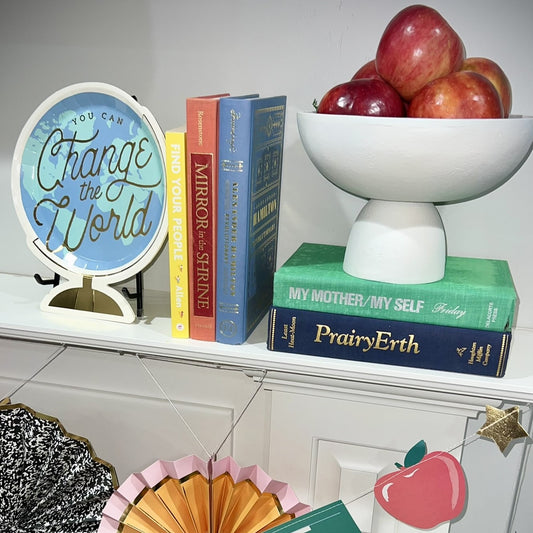 Decorative shelf with books, a 'Change the World' sign, and a bowl of apples.