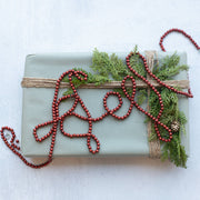 Gift wrapped in green paper with red beads and greenery on a white background