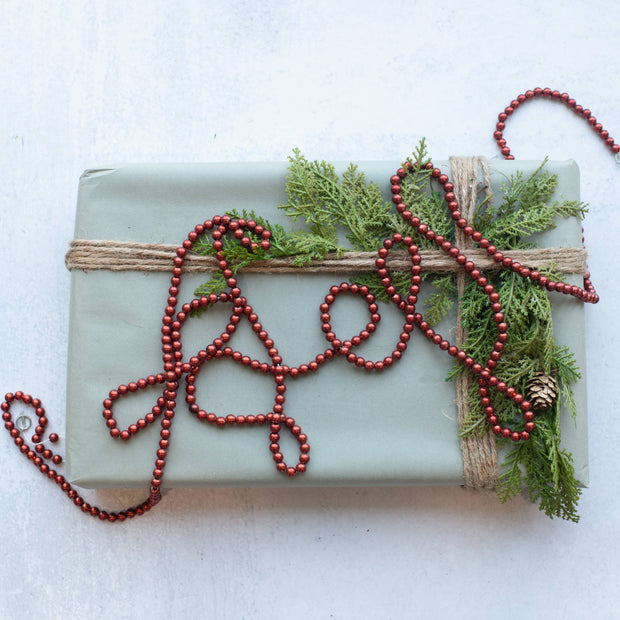 Gift wrapped in green paper with red beads and greenery on a white background