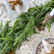 Decorative table setting with garland greenery, plates, and napkins on a lace tablecloth.