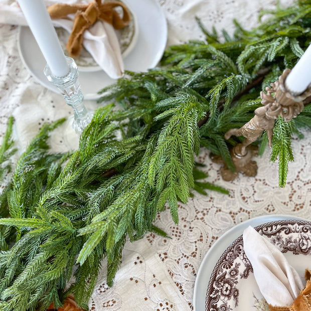 Decorative table setting with garland greenery, plates, and napkins on a lace tablecloth.