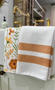 Decorative towel with floral design and stripes hanging on a bathroom rack.