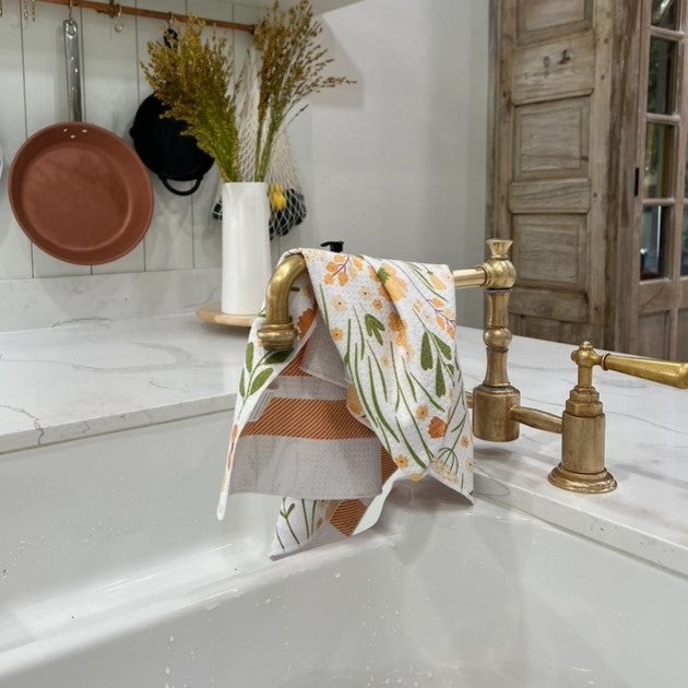 Kitchen sink with gold faucet and floral towel, wooden cabinets in the background