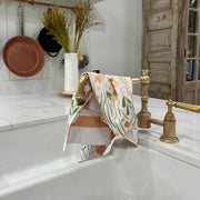 Kitchen sink with gold faucet and floral towel, wooden cabinets in the background
