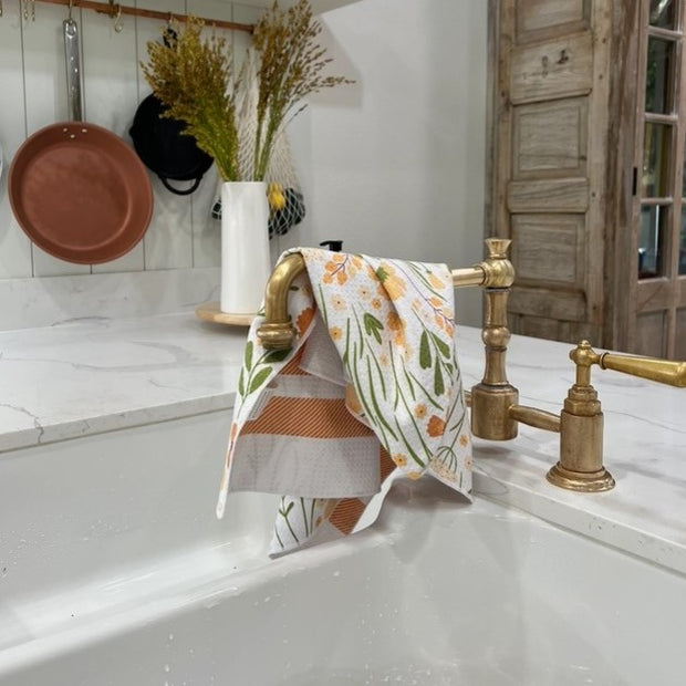 Kitchen sink with gold faucet and floral towel, wooden cabinets in the background