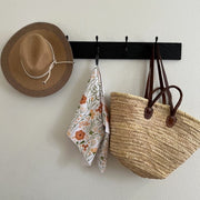 Hat, floral towel, and woven bag hanging on a black wall hook against a white wall.