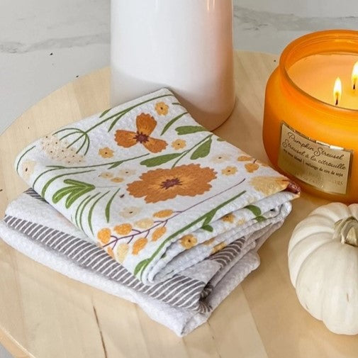 Folded floral towel with a lit candle and small pumpkin on a wooden surface