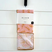 Packaged towel with floral design and 'Bloom' branding on a white wooden background