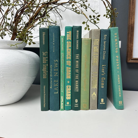 A collection of decorative books with green covers displayed on a shelf, with a decorative item partially visible to the left.