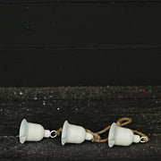 Three white metal bells on a string against a black background