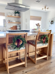 Two wooden bar stools with decorative cushions and wreaths in a kitchen setting.