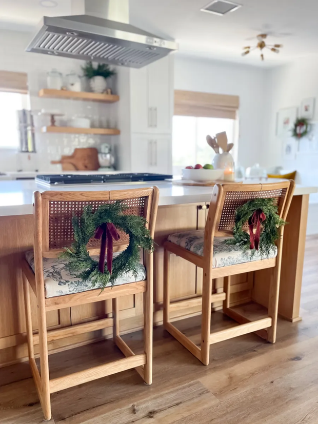 Two wooden bar stools with decorative cushions and wreaths in a kitchen setting.