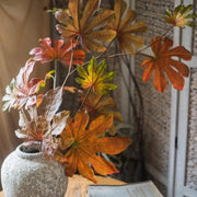 Decorative plant with autumn-colored leaves in a textured pot on a wooden surface.