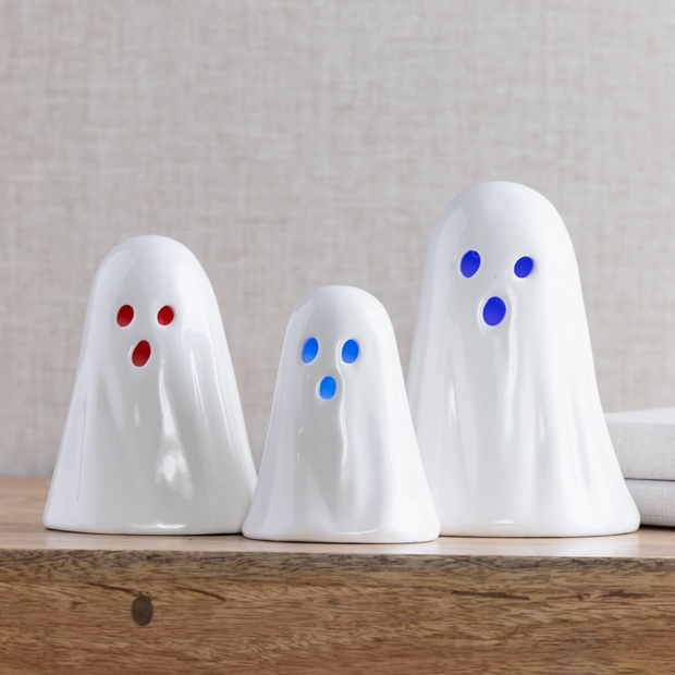 Three white ghost-shaped night lights with colored eyes on a wooden surface.
