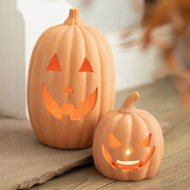 Two carved pumpkins with lit candles on a wooden surface.