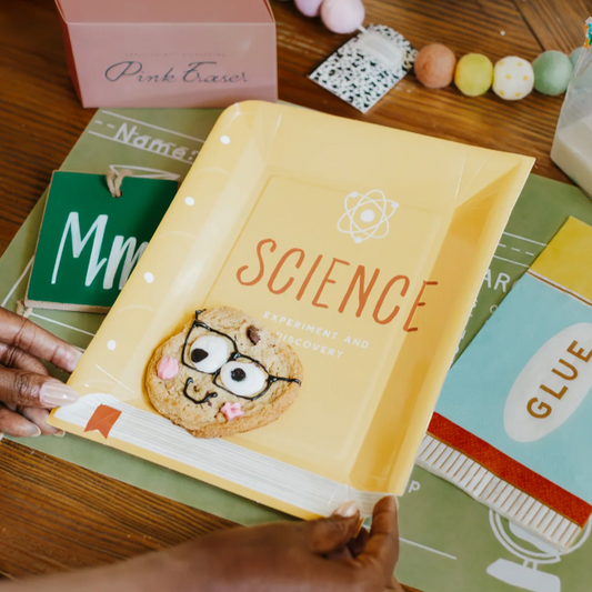 Yellow book titled 'Science' held by a hand on a wooden surface with educational materials.