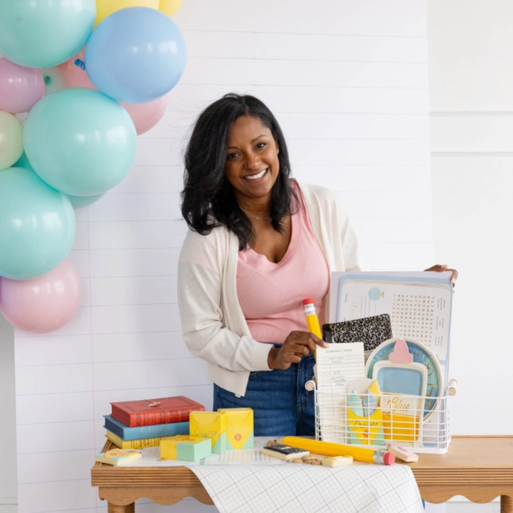 Woman holding a product with balloons and stationery items in the background